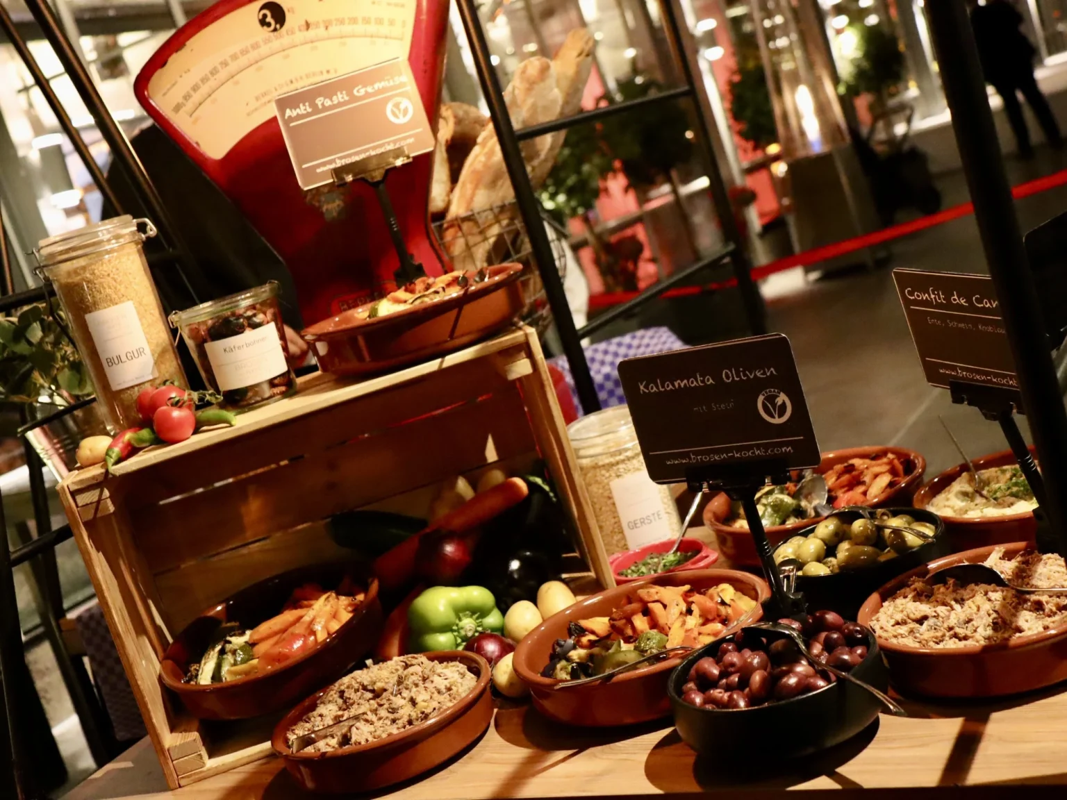 Übersicht eines Antipasti-Buffets mit Holzkiste, Waage und Schälchen