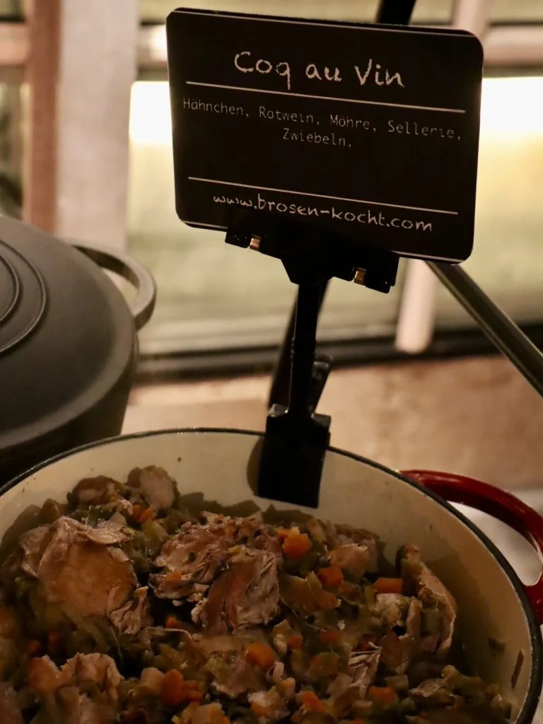 Gusseisentopf mit Coq au Vin und Schild am warmen Buffet