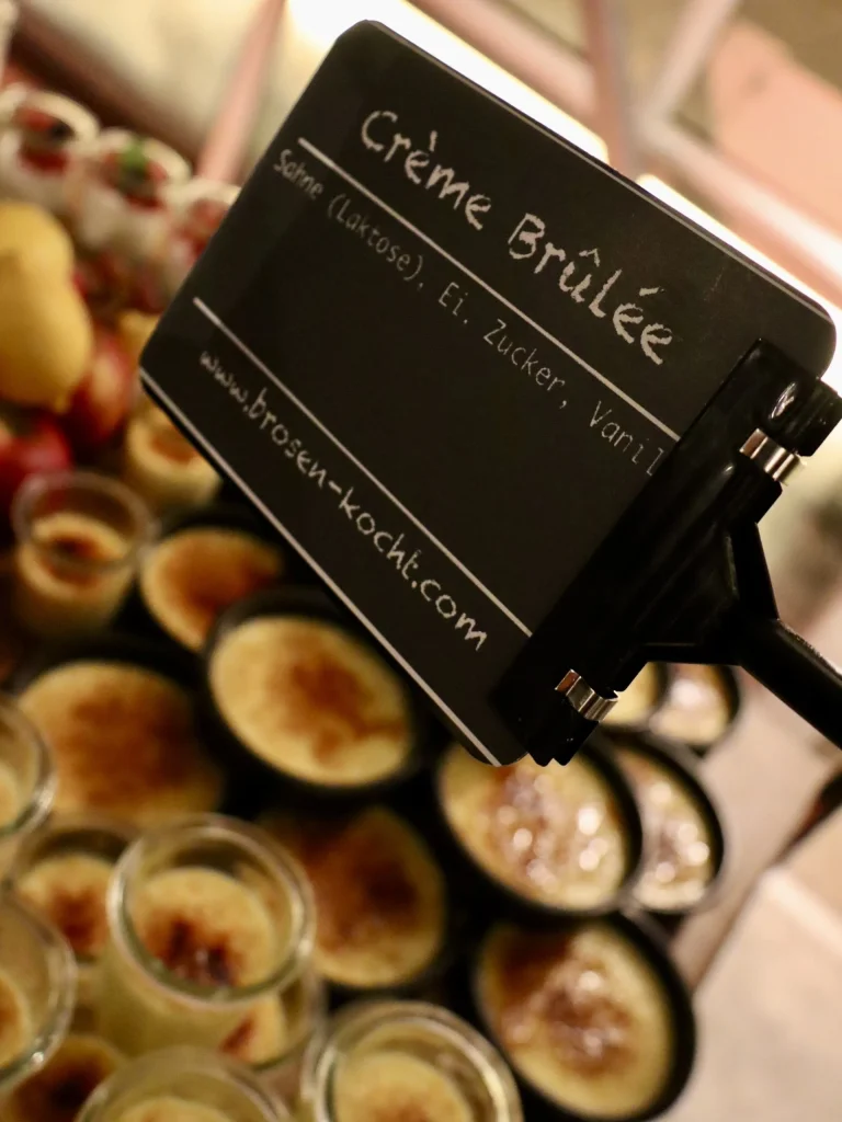 Schild „Crème Brûlée" über mehreren Crème-Brûlée-Gläsern am Dessert-Buffet