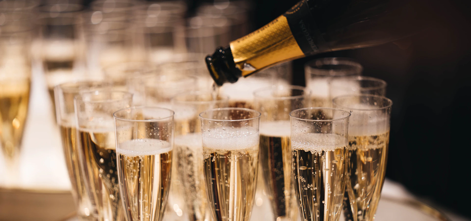 Sekt wird in bereitstehende Gläser eingeschenkt