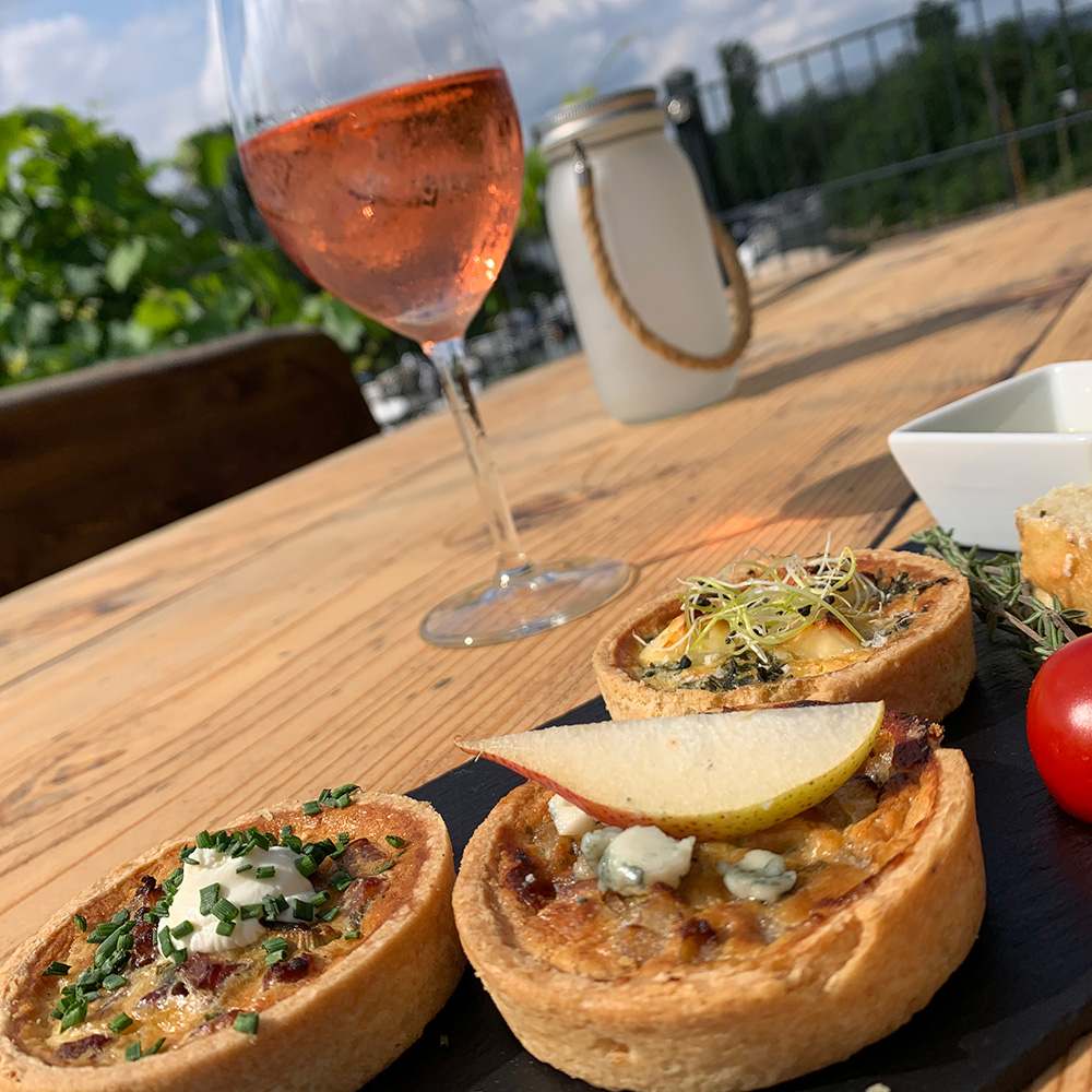 Gefüllte Tartelettes und ein Glas Roséwein auf einem Holztisch im Freien
