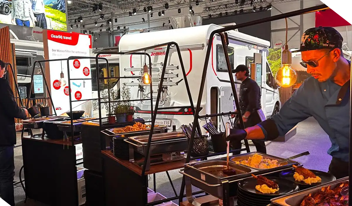 Koch richtet an einer Catering-Station auf einem Messestand warme Speisen auf Tellern an