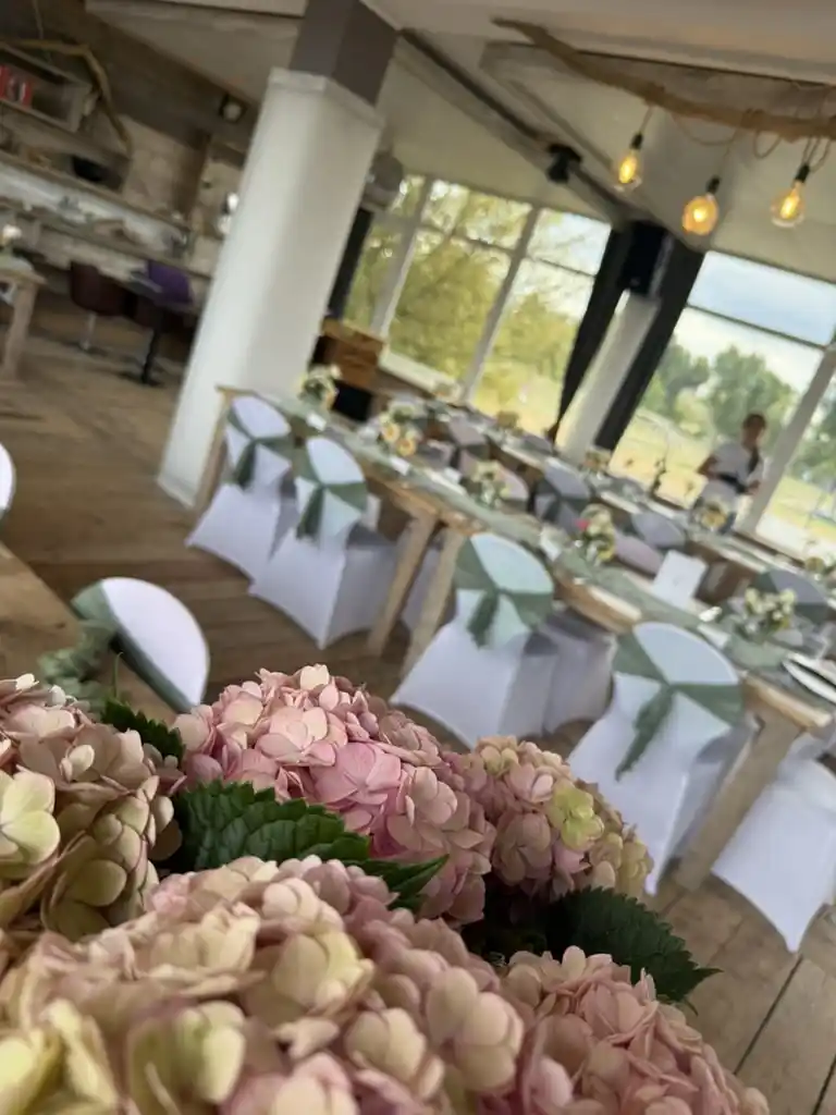 Hochzeitlich gedeckte Tafeln mit Stuhlhussen und Hortensien im Rheinclub 297 vor großer Fensterfront